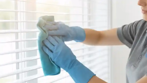 Professional cleaner wiping down white venetian blinds in bright room